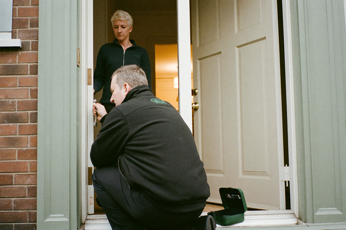 A locksmith working on a front-door lock while the customer waits in the hallway.