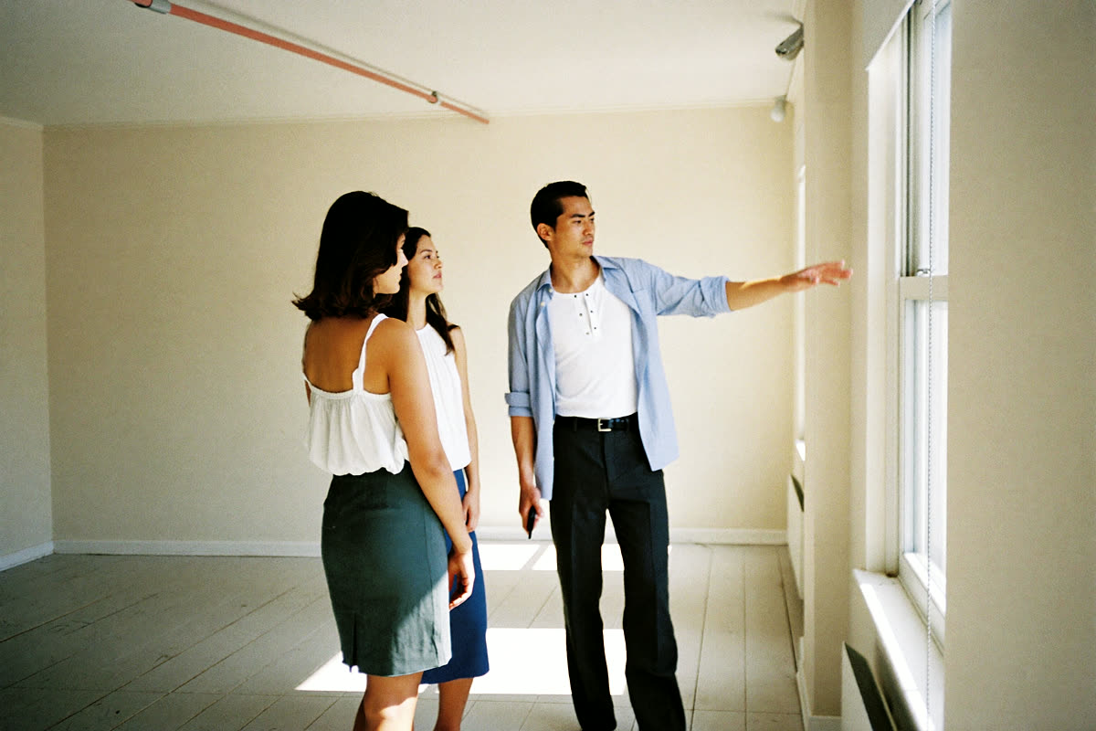 A letting agent showing a couple around a bright empty flat.